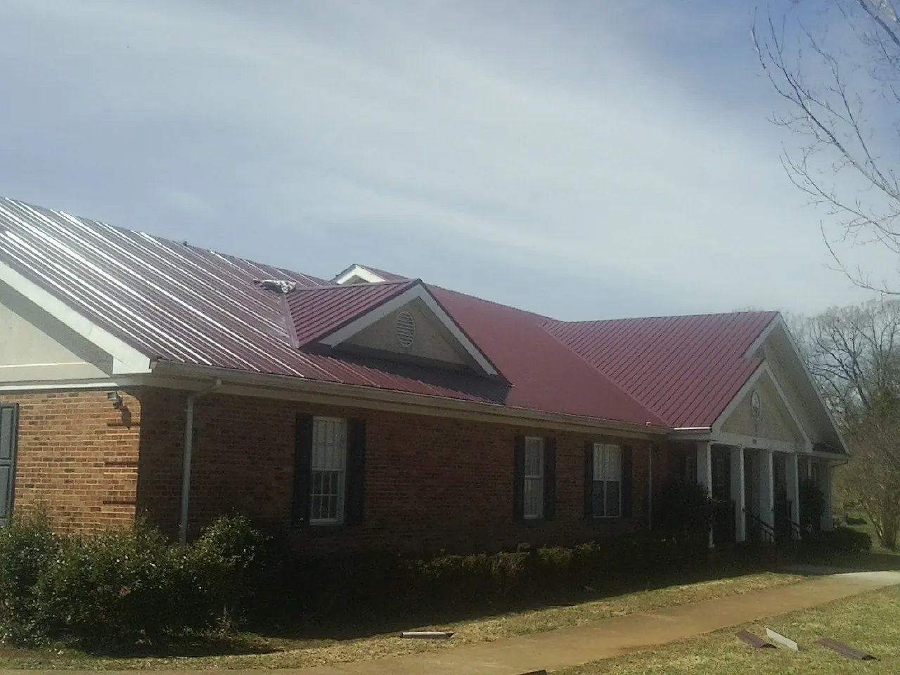 Red metal roof with gabled entries on a long brick building, from a Hail Damage Roof Repair job in Mauldin