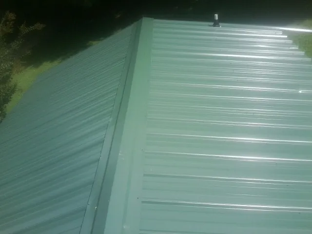 New green metal panels meeting at the ridge of a roof — Flat Roof Repair work by our crew in Mauldin