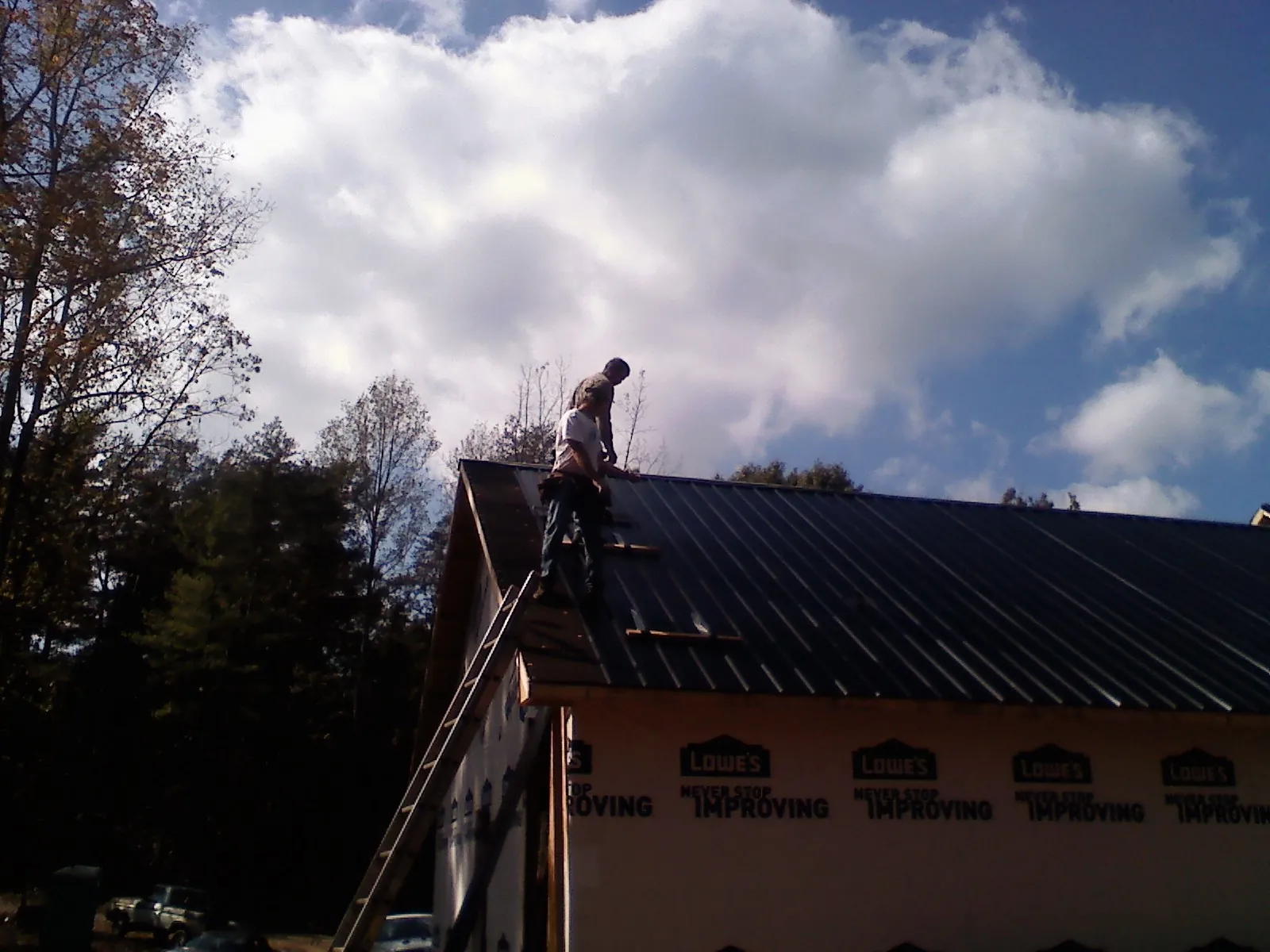Roofer fastening dark metal panels high against a cloudy sky, from a Roof Inspection job in Mauldin
