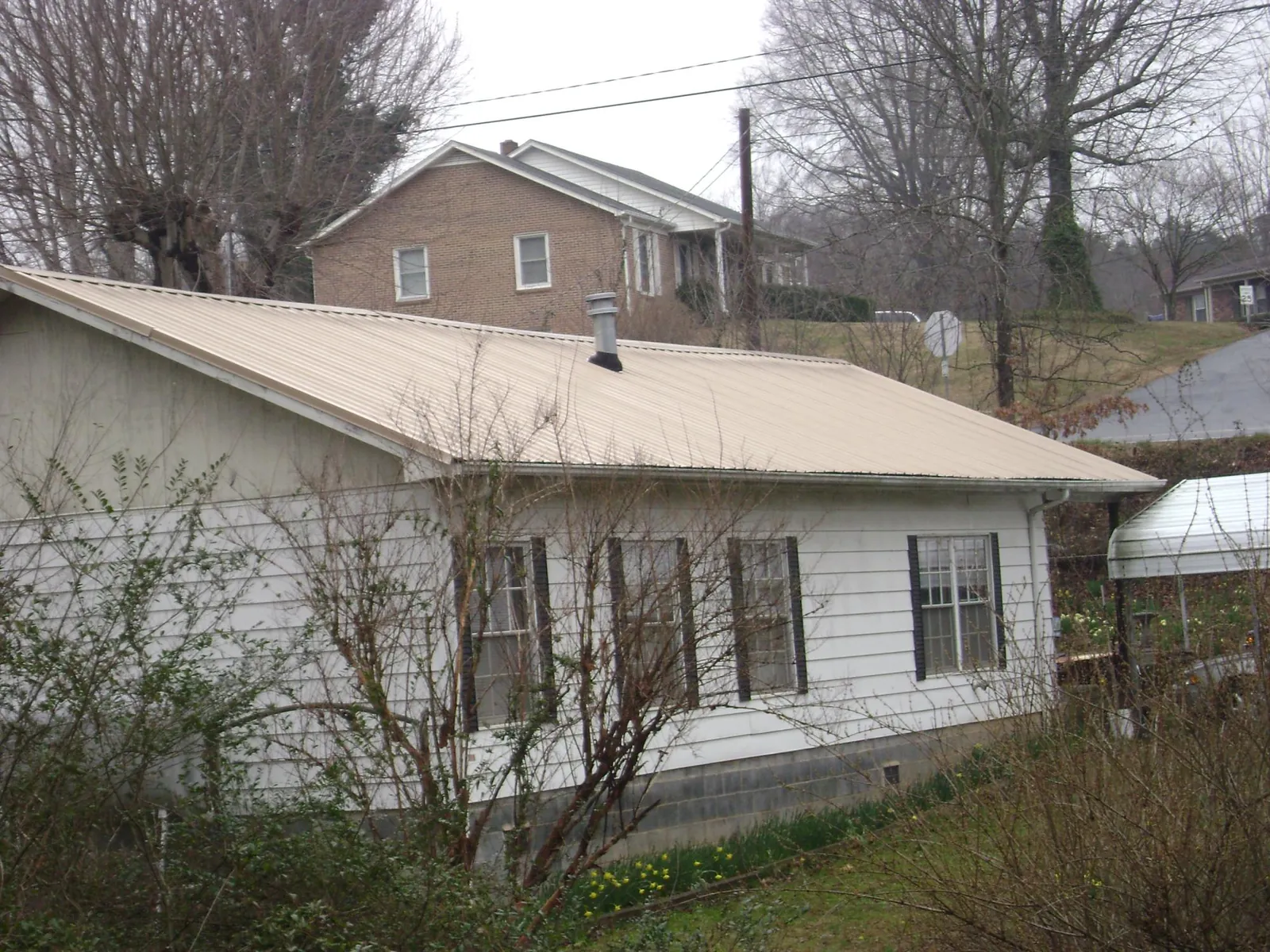 Tan metal roof on a white sided house set into a hillside — Commercial Roofing by Roofing Brothers in Mauldin
